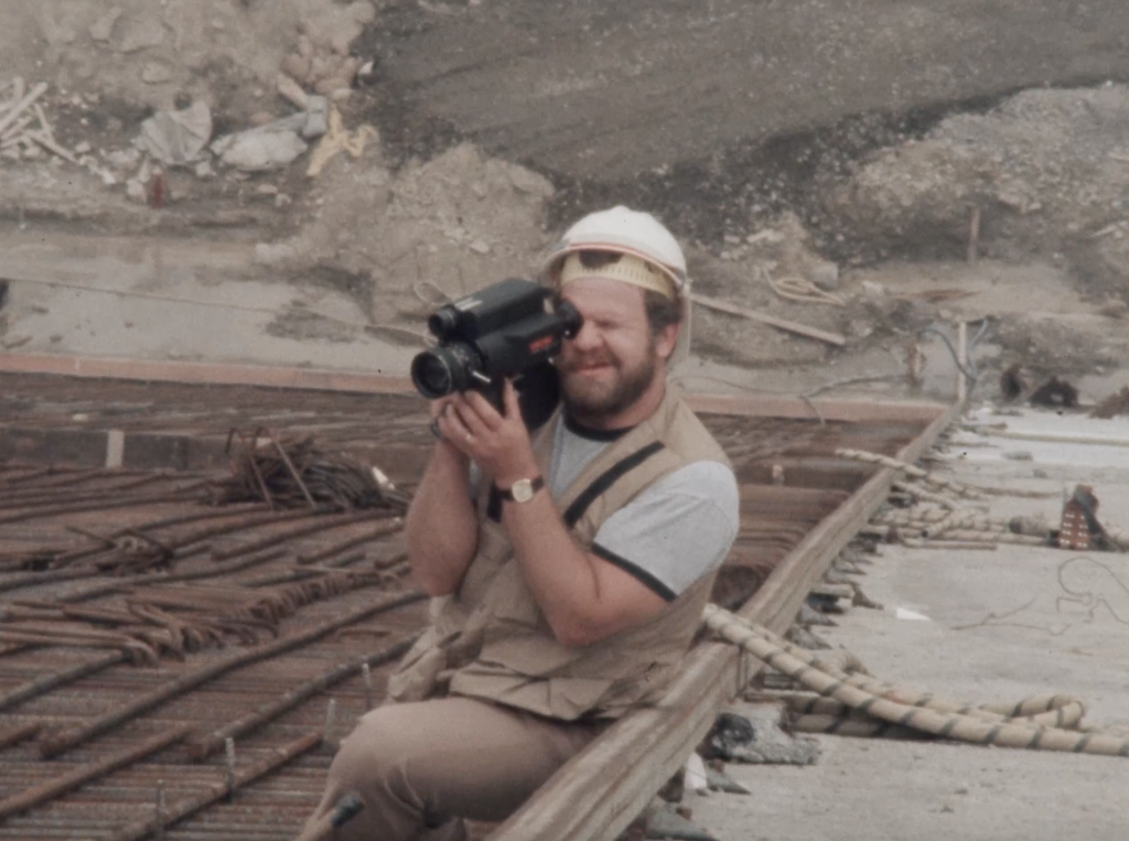Construction worker wearing a hard hat and filming with a 16mm Scoopic camera