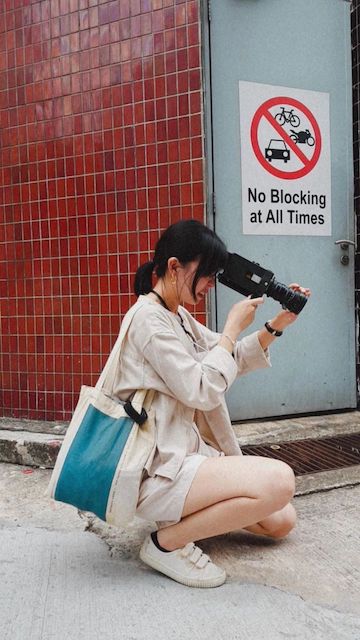 A person crouches on the ground with a Super 8 camera at their eye; a sign in the background reads "No Blocking at All Times"