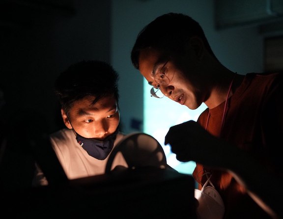 Close-up of two people in a dark room bending over a film projector